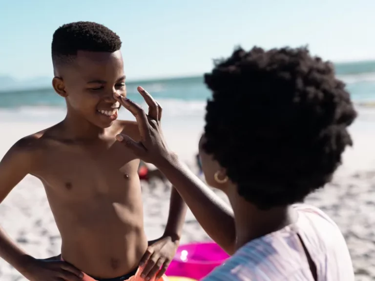 a black woman applying sunscreen in a black young boy